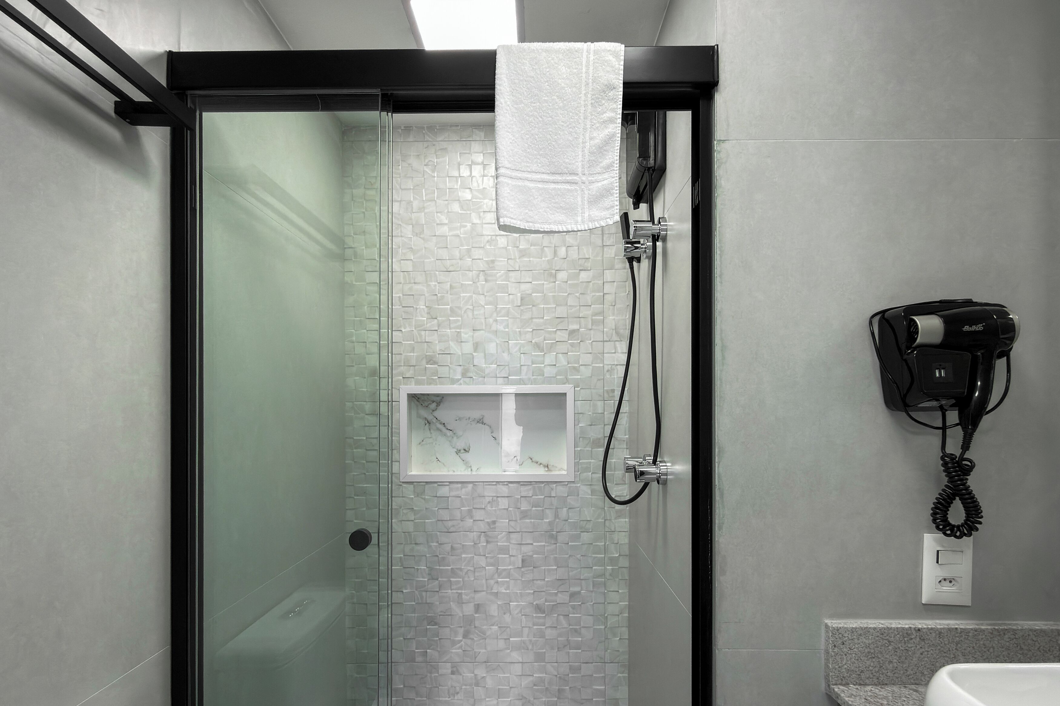 Ein modernes Badezimmer mit einer Duschkabine aus Glas, einem Marmorwaschbecken und einem an der Wand befestigten Föhn.