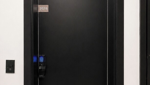 Een moderne lift met een digitaal keypad slot, een bordje met het kamer nummer 202 B, en een effen muur.