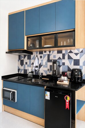 A kitchen with blue cabinets, a black countertop, a coffee machine, and a microwave. - Premium Studio 5 min from CGH, Gym and Coworking (São Paulo)
