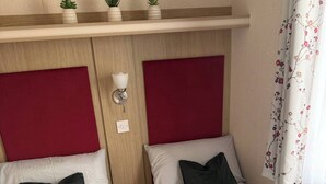 Ein Hotelzimmer mit zwei Betten, einem Holzkopfende, einem Nachttisch, einer Wandleuchte und einem blumigen Vorhang.