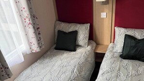 Ein Zimmer mit zwei Betten, jeweils mit blumigem Bettbezug, einem roten Kopfteil und einer kleinen Ablage mit Topfpflanzen.