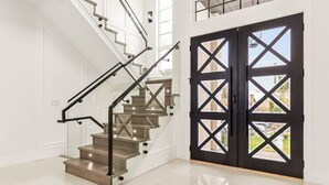 Un escalier avec des rampes en verre et une porte noire ornée de motifs en forme de croix.