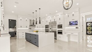 Une cuisine moderne avec des meubles blancs, des appareils en acier inoxydable et des luminaires suspendus.