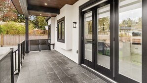 Un espace extérieur abrité comprenant une table de patio, un plafond en bois et une porte-fenêtre coulissante donnant sur un garage.
