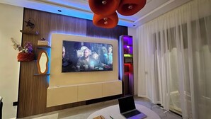 A modern living room with a large flat-screen TV, a laptop on a round table, and a unique ceiling light fixture. - Studio Luxe-Wintering-Pool/M'Avenue/2min Station (Marrakesh)