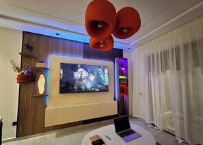 A modern living room with a large flat-screen TV, a laptop on a round table, and a unique ceiling light fixture. - Studio Luxe-Wintering-Pool/M'Avenue/2min Station (Marrakesh)