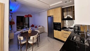 A modern kitchen with a built-in oven, a dining area with a round table and chairs, and a living area with a sofa and a TV. - Studio Luxe-Wintering-Pool/M'Avenue/2min Station (Marrakesh)