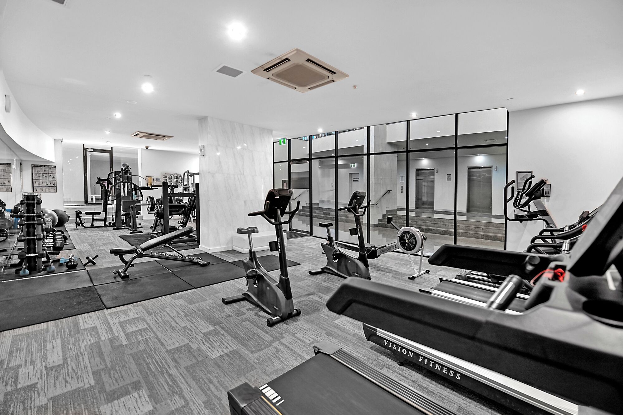 A modern gym with various exercise equipment, including treadmills and stationary bikes, and a weightlifting area.