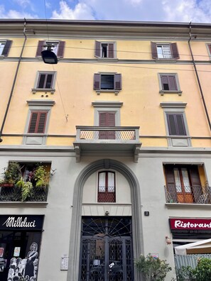 Ein Gebäude mit mehreren Fenstern, einem Balkon mit Geländer und einer Tür mit aufwendiger Gestaltung.