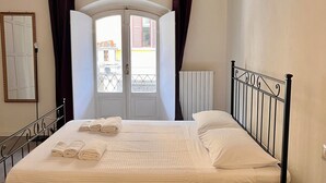 Ein Schlafzimmer mit Bett, einem fenster mit Vorhängen, einer Heizung und Holzboden.