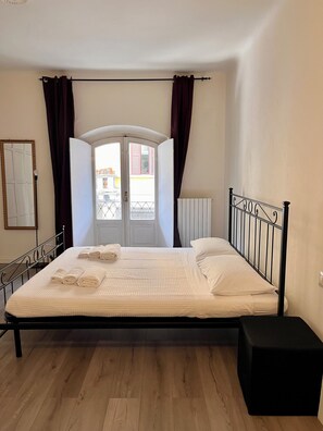 Ein Schlafzimmer mit Bett, einem fenster mit Vorhängen, einer Heizung und Holzboden.