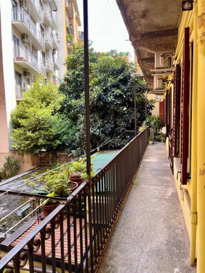 A narrow balcony with a metal railing, potted plants, and a view of a multi-story building with balconies. - Charming Cozy flat in the Heart of Porta Venezia (Milan)