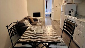 Ein kompakter Wohnbereich mit Esstisch, Stühlen, einer Couch, einem Fernseher und einer Küchenzeile.