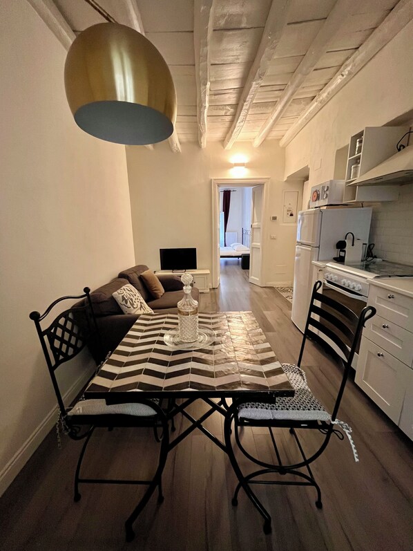 A compact living space with a dining table, chairs, a sofa, a television, and a kitchenette. - Charming Cozy flat in the Heart of Porta Venezia (Milan)