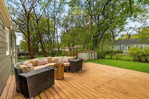 Eine überdachte Terrasse mit Holzboden, Gartenmöbeln und einem kleinen Geräteschuppen.