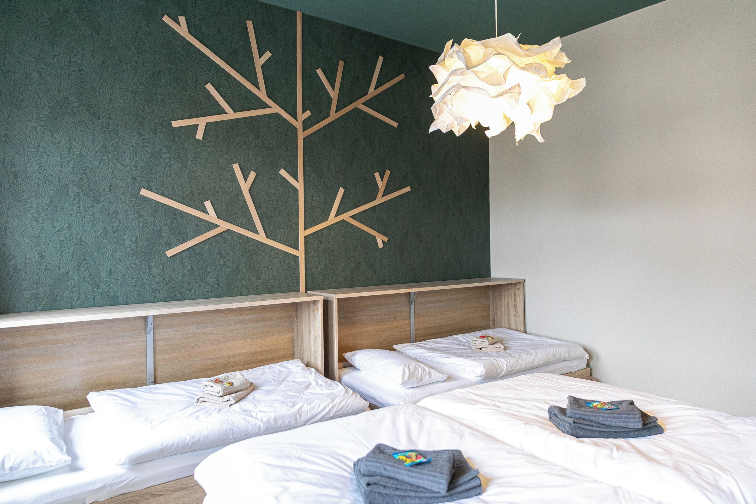 A hotel room with two beds, a wooden branch wall decoration, and a hanging light fixture.