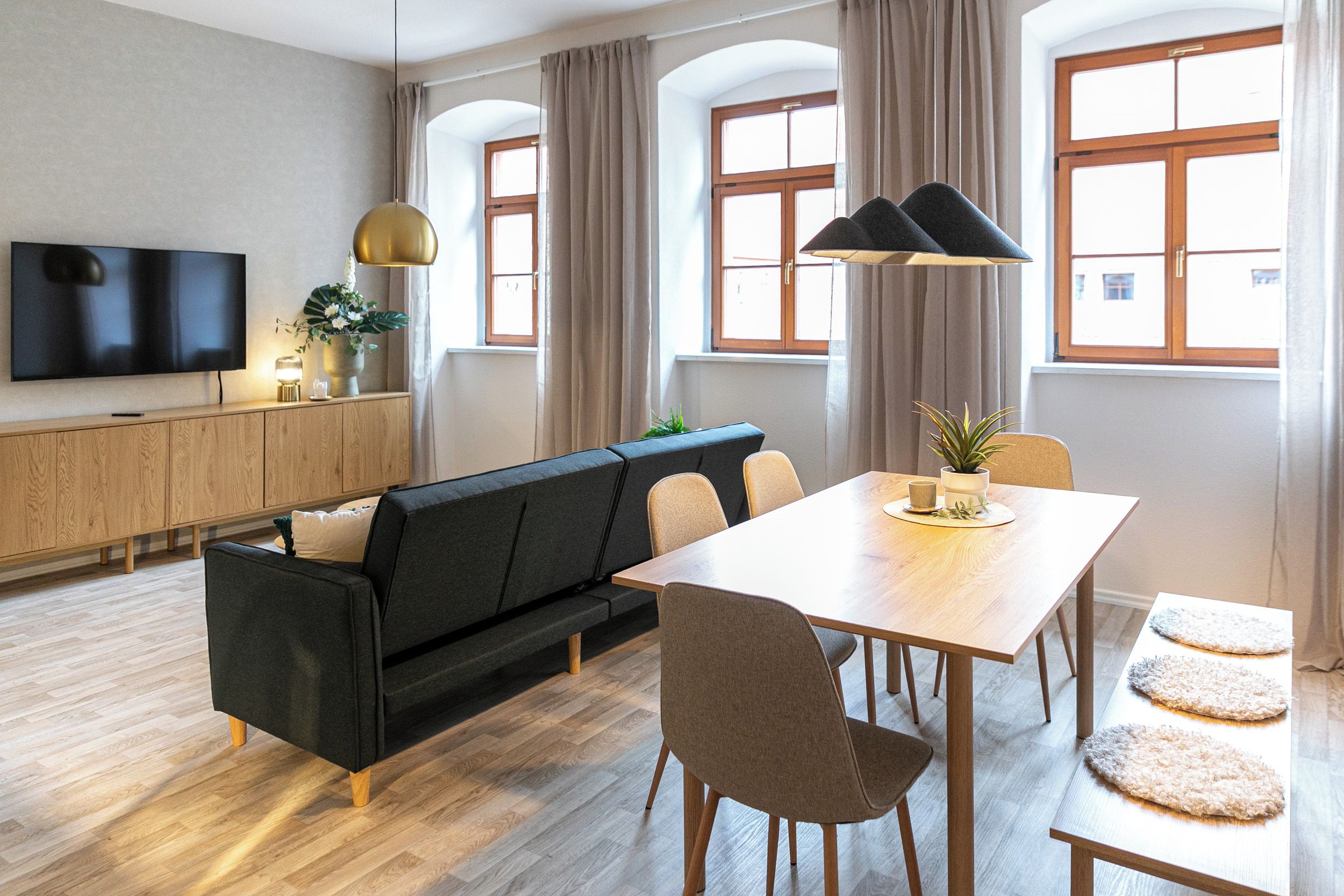 Una sala de estar moderna con sofá, mesa de comedor, sillas, televisor y una planta.