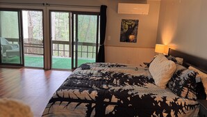 Um quarto com cama, porta de vidro deslizante para um pátio, um quadro na parede e uma luminária.