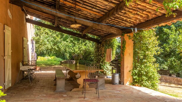Eine Terrasse im Freien mit Tisch und Stühlen, umgeben von viel Grün.