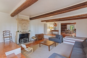 A spacious living room with a fireplace, a sofa, a coffee table, and a dining area visible through an open door. - Holiday Home 'Grand Mas Provencal - 9 Ch - 18 Per' with Mountain View, Private Pool and Wi-Fi (La Farlède)