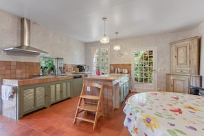 A kitchen with a central island, a dining area with a chair, and a bed with a floral bedspread. - Holiday Home 'Grand Mas Provencal - 9 Ch - 18 Per' with Mountain View, Private Pool and Wi-Fi (La Farlède)