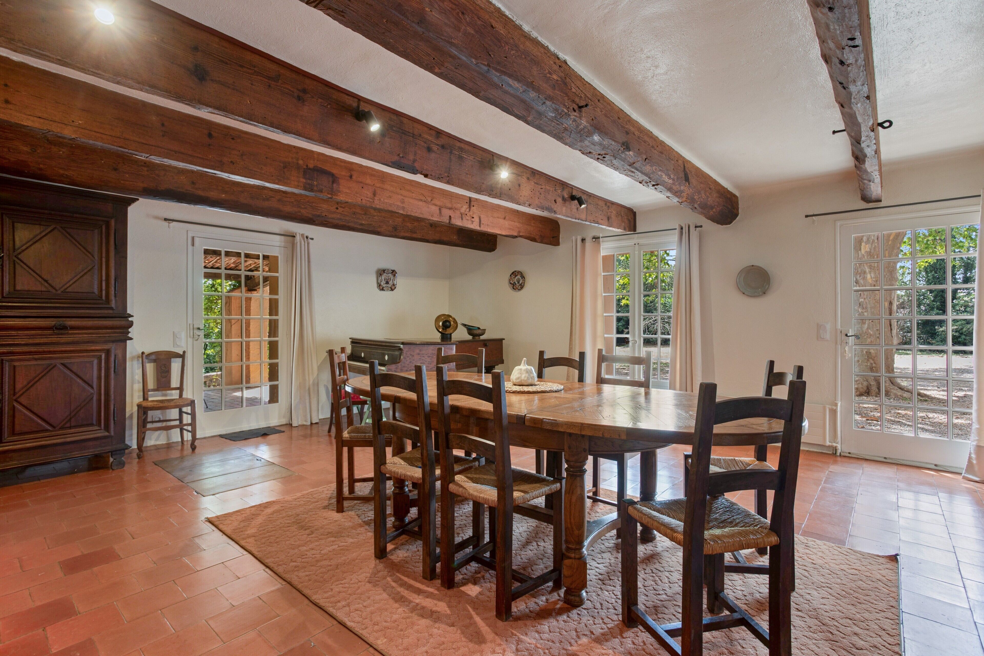 Un comedor con una mesa y sillas de madera, un armario y vistas a través de puertas de vidrio.