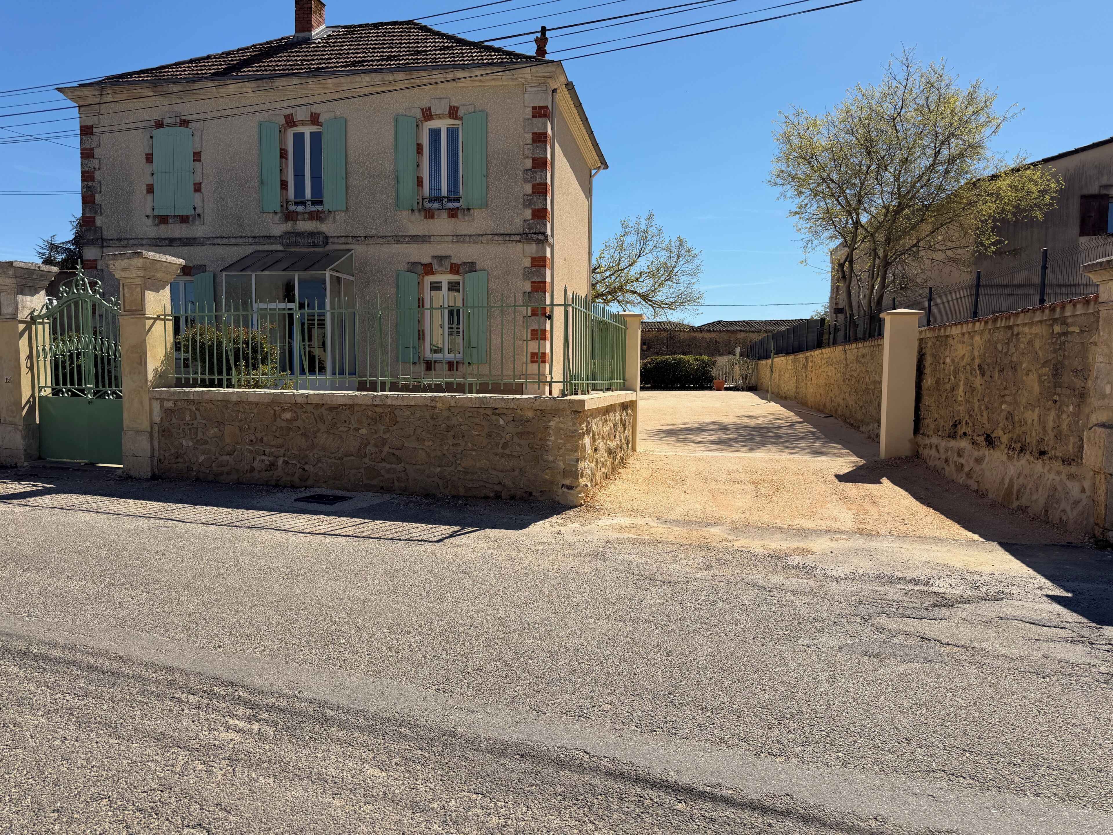 A two-story building with a stone facade, a metal gate, and a paved driveway.