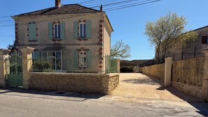 Edifici de dues plantes amb façana de pedra, una reixa de metall i un carrer d'accés pavimentat.
