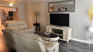 Ein Wohnzimmer mit einer Couch, einem Fernseher auf einem Schrank, einer Lampe und einer Vase mit Blumen.