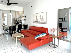 A modern living room with a red sofa, a dining area with chairs, a kitchen in the background, and a large mirror reflecting the room. - Spacious 3br Drenched with light Gem Beach Walk Loíza · Quiet & Airy (San Juan)