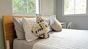 Un lit avec une tête de lit en bois, une couvre-lit blanche matelassée et plusieurs oreillers.