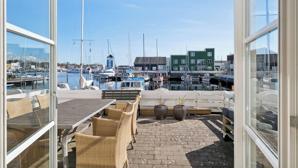 Un porto turistico con barche, un pontile di legno, sedie in vimini e un edificio verde.