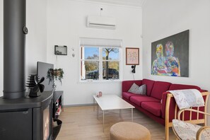 A living room with a red sofa, a white table, a wooden chair, a black stove, and a large painting on the wall. - Holiday apartment in Øer Maritime Ferieby (Ebeltoft)