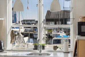 A kitchen with a large window, a sink, and a hanging light fixture. - Holiday apartment in Øer Maritime Ferieby (Ebeltoft)