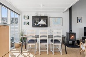 A dining area with a table, chairs, a hanging light fixture, a map on the wall, and a wood-burning stove. - Holiday apartment in Øer Maritime Ferieby (Ebeltoft)