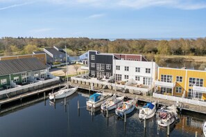 A marina with boats docked, a dock with a covered seating area, and buildings with large windows and a white fence. - Holiday apartment in Øer Maritime Ferieby (Ebeltoft)