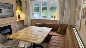 Une pièce avec une table en bois, un canapé en cuir marron, une fenêtre avec des rideaux et un tableau encadré au mur.