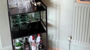 A black metal bar cart with multiple shelves, containing various bottles and glasses. - Your Private Cotswolds Castle – Fairytale Stay in a Honey-Stone Village (Banbury)