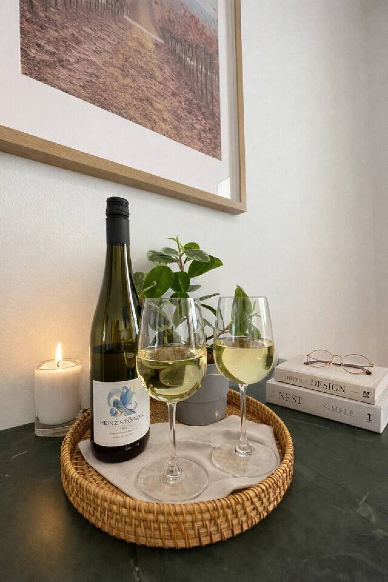 Vinflaske, to glas, et lys, en plante og bøger på et bord.