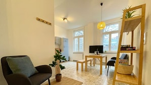 Een woonkamer met een bank, een salontafel, een televisie, een plant, een houten laddenplank en een vloer met een patroon.