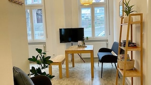 Een kleine, goed verlichte kamer met een televisie, een houten tafel, een stoel, een vloerlamp en een boekenkast.
