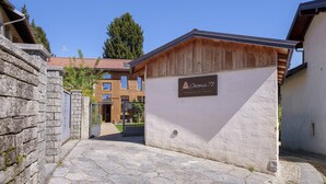 Un patio empedrado con un edificio de madera identificado como 'Osteria 71' y un muro de piedra.