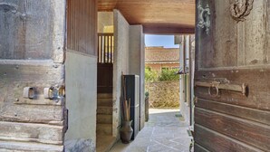 Una puerta de madera que da a un área empaveda de piedra con una reja metálica, una escalera y vistas de un edificio con tejado de tejas.