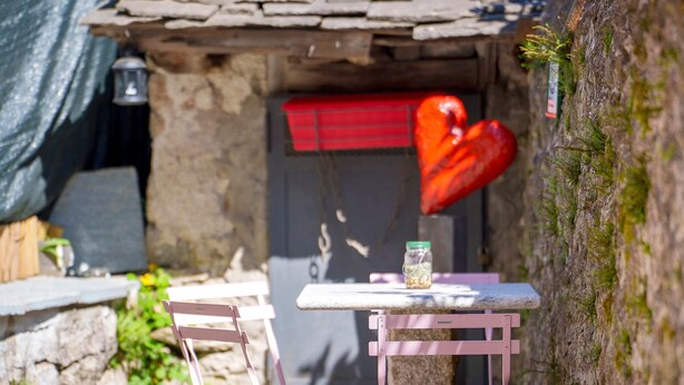 Un área de estar al aire libre con aspecto rústico, que incluye una mesa y sillas de piedra, una decoración con forma de corazón y un farol.