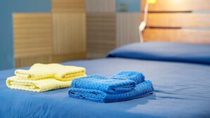 Una cama bien hecha con toallas azules y amarillas, un cabecero de madera y una lámpara fijada a la pared.