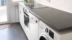 Eine moderne Küche mit weißen Schränken, einer Edelstahl-Arbeitsplatte, einem Backofen und einer Waschmaschine.