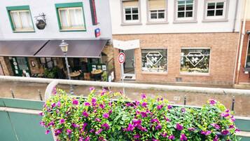 A balcony with hanging flower baskets and a view of a street with buildings and a no parking sign.