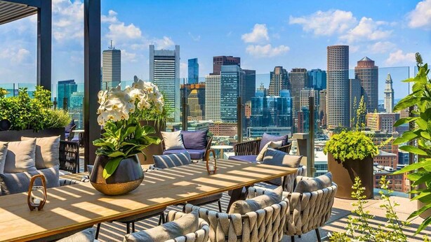 A rooftop terrace with a city skyline view, furnished with a table and chairs, and potted plants. - Luxury Seaport Stay | Rooftop & Pool (Boston, MA)