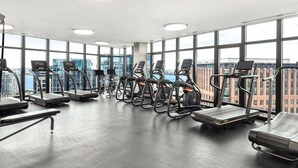 A gym with treadmills, elliptical machines, and stationary bikes, large windows with a city view, and a polished concrete floor. - Luxury Seaport Stay | Rooftop & Pool (Boston, MA)