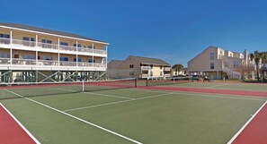 Un court de tennis avec un filet, entouré d’immeubles dotés de balcons, sous un ciel dégagé.